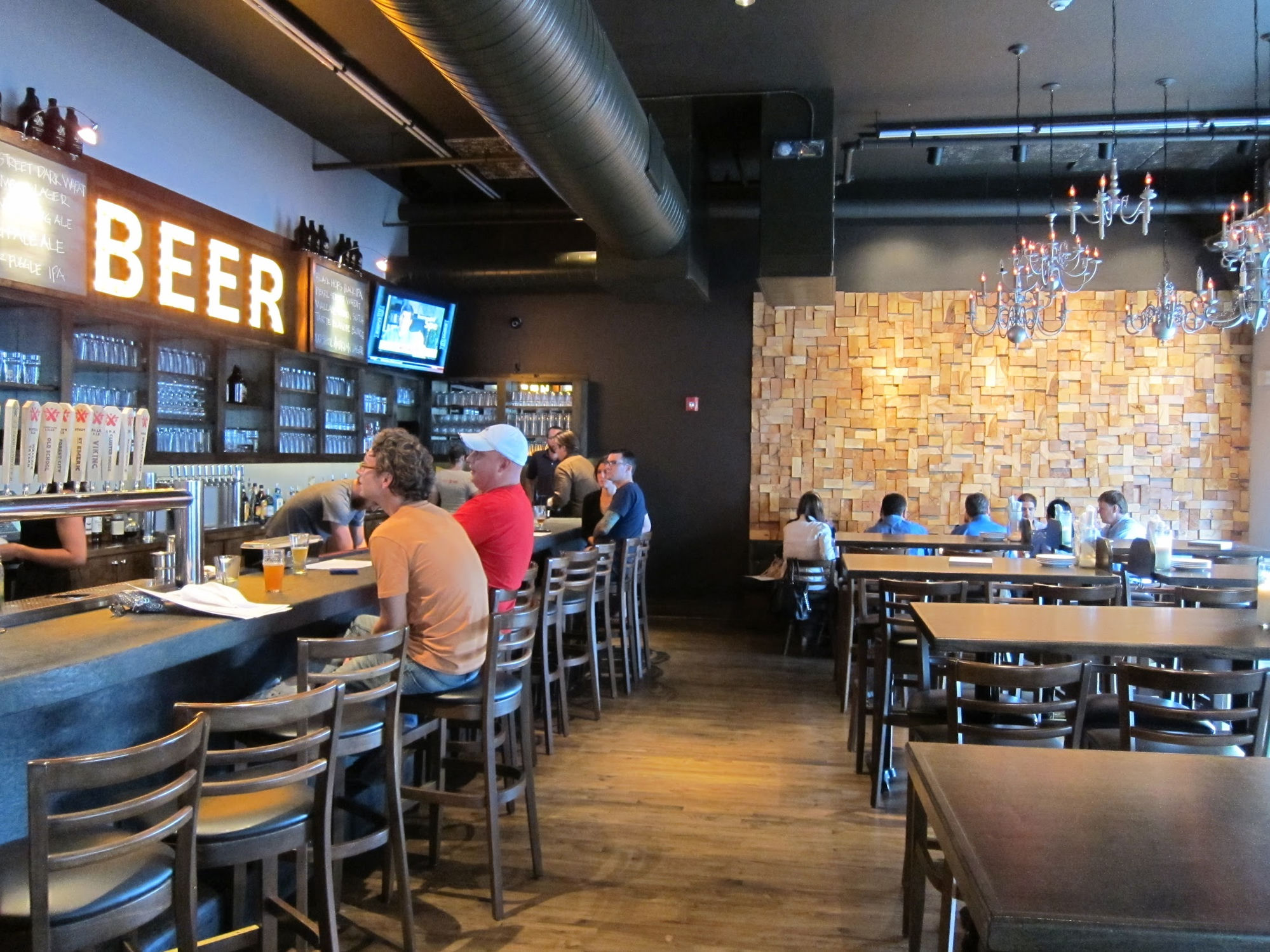 Market Garden Brewery bar and dining area, with a glowing BEER sign, tap handles, and a textured wood-block accent wall