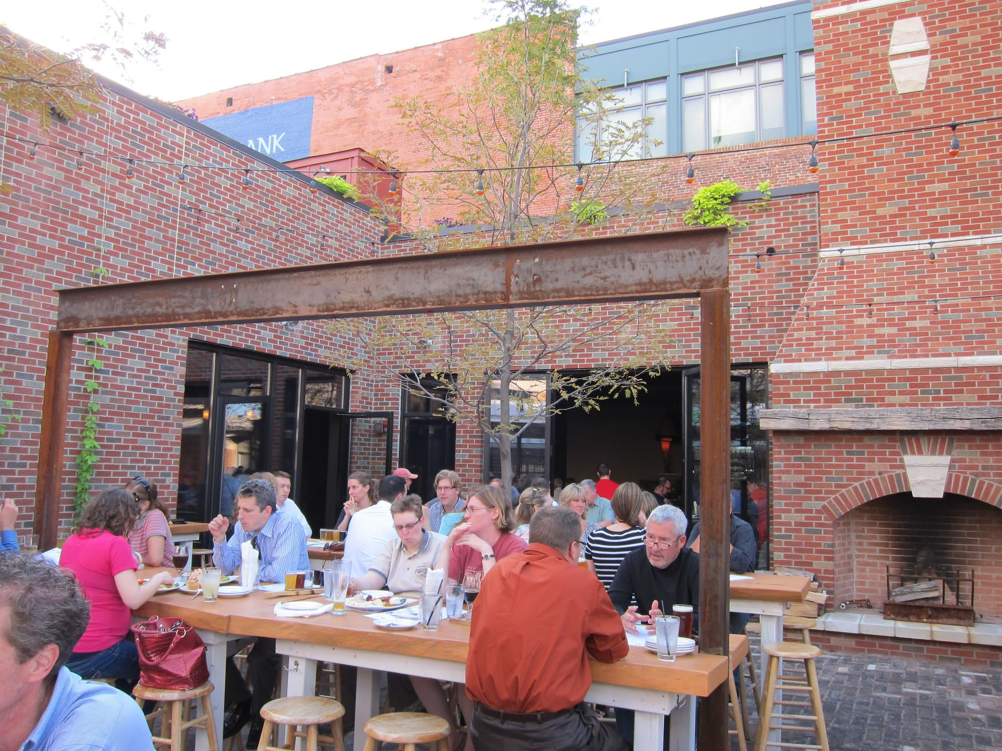 Market Garden Brewery beer garden with diners at communal tables, brick walls, string lights, and an outdoor fireplace