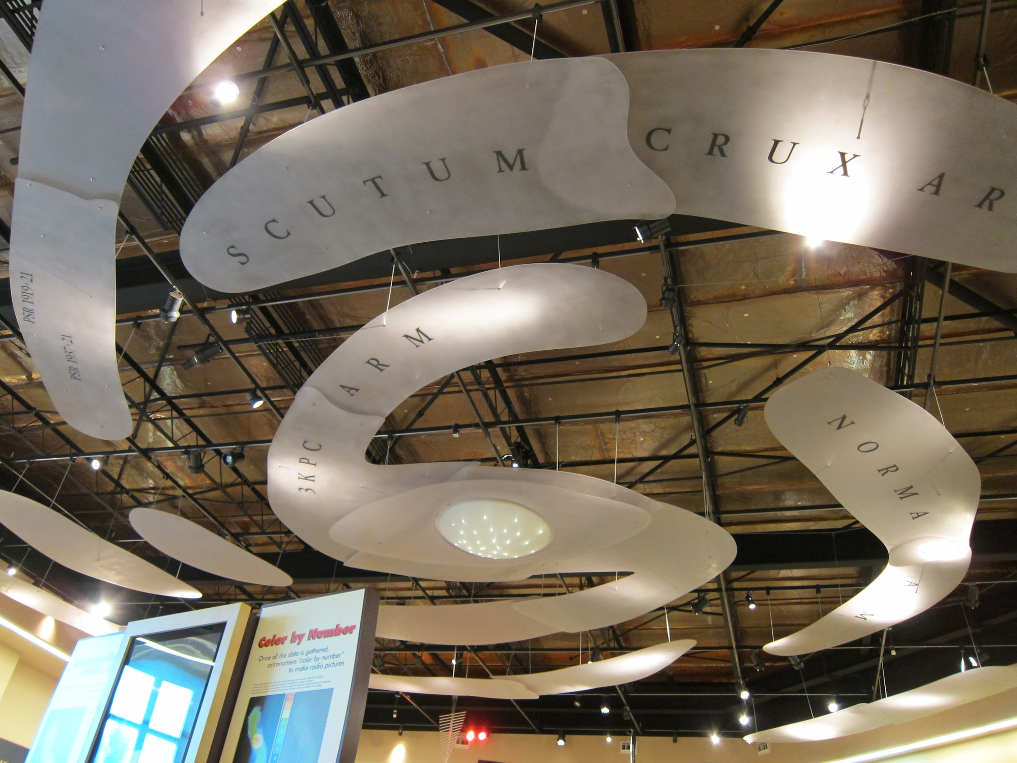 Large-scale model of the Milky Way's spiral arms suspended from the ceiling of the NRAO visitors center, with arms labeled Scutum-Crux, 3KPC, and Norma