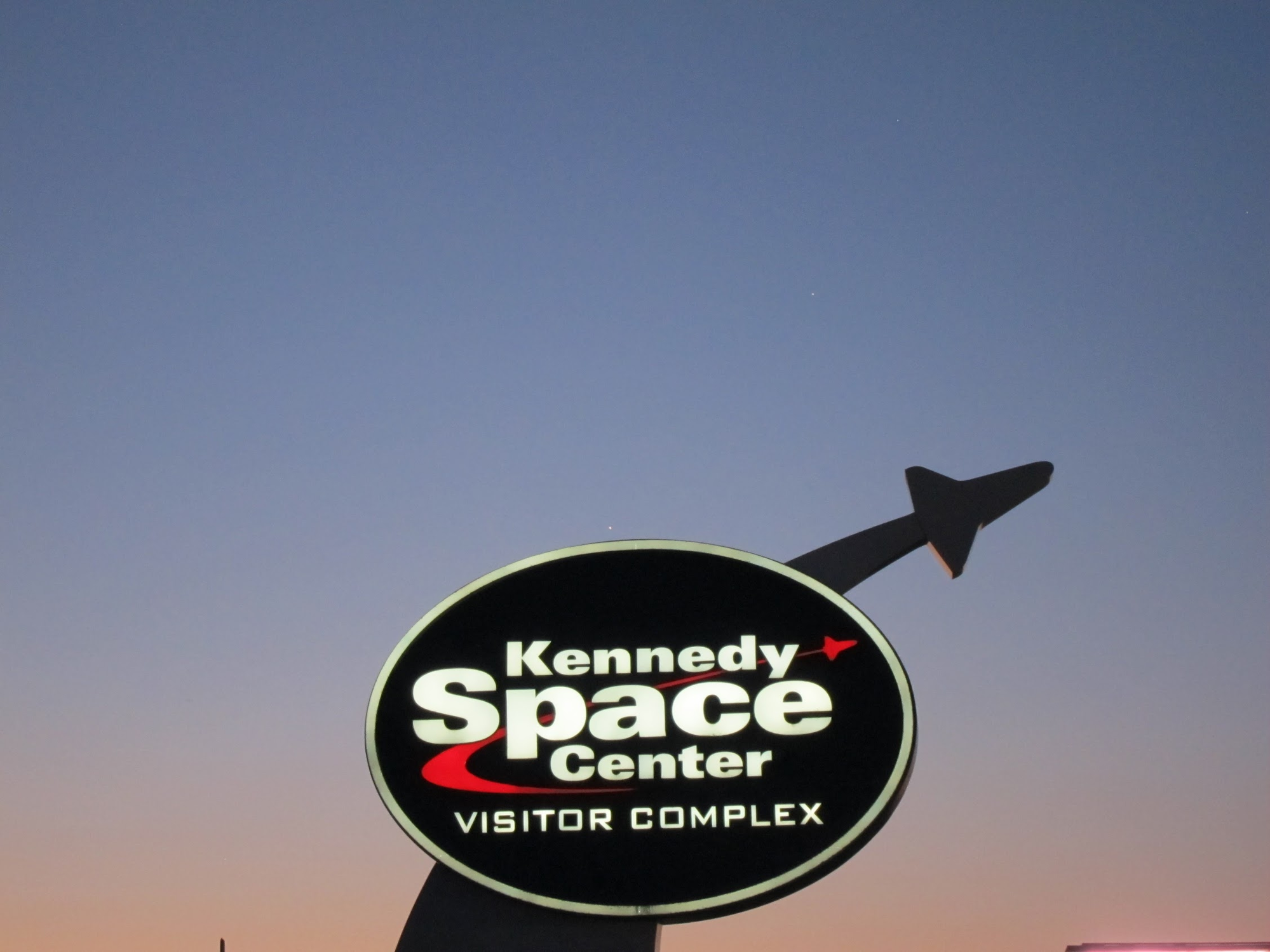 Kennedy Space Center sign at dusk with shuttle silhouette against twilight sky