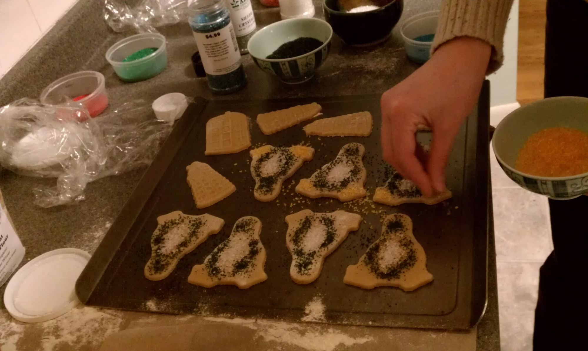 Susan decorating Tux penguin cookies with black and white sugar sprinkles, with bowls of colored sugar in the background