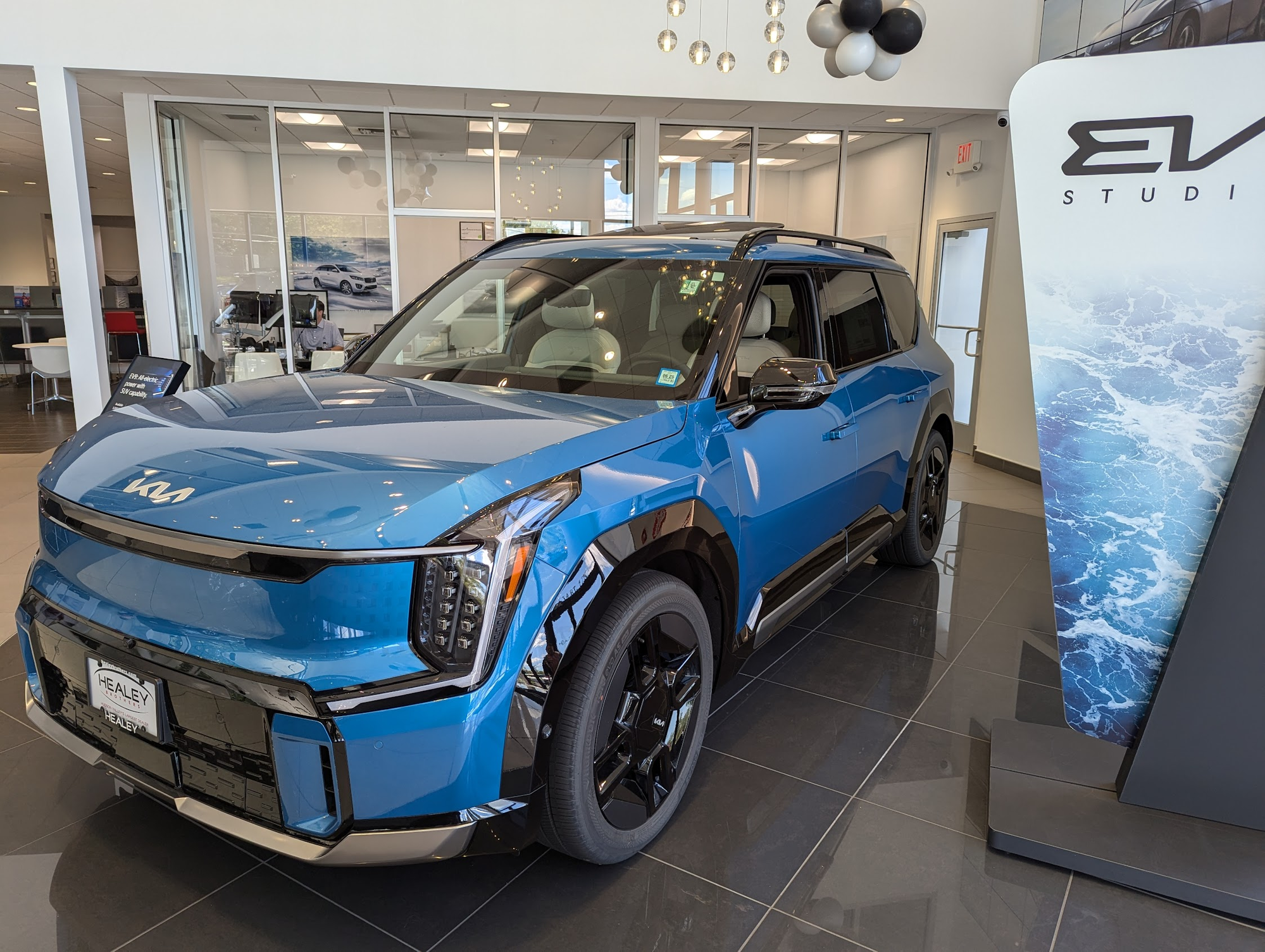 Blue Kia EV9 on the showroom floor at Healey Kia, next to an EV Studio display